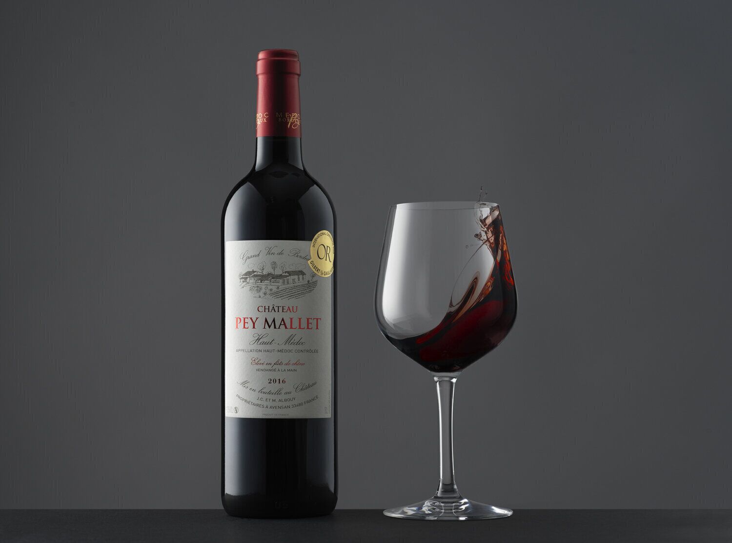 A bottle of Château Pey Mallet Haut-Médoc wine and a glass of wine.