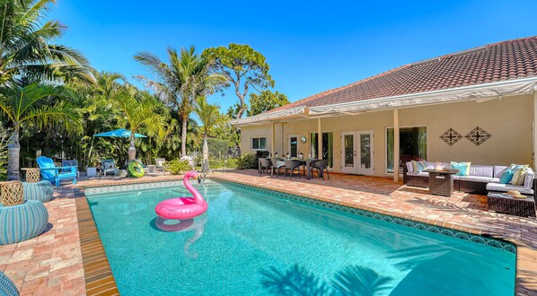A swimming pool with a pink flamingo float, outdoor furniture, and a covered patio area.