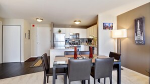 Een moderne keuken met witte kasten, roestvrijstalen apparatuur en een eethoek met een glazen tafel en stoelen.