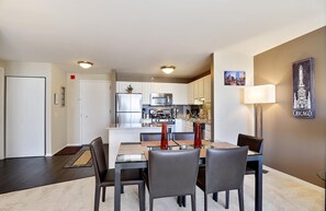 A modern kitchen with white cabinets, stainless steel appliances, and a dining area with a glass table and chairs. - 52nd Floor Penthouse with Skyline Views and Pool (Chicago)