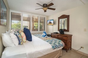 A bedroom with a bed, a ceiling fan, a dresser, a mirror, and a TV.