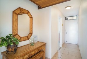 A hallway with a wooden console table, a large mirror, and a potted plant. - Kamaole Sands #5-313 Idyllic Ocean Courtyard View, Across from Beach! A/C (Kihei)