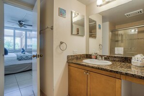 A bathroom with a granite countertop sink, wooden cabinets, a ceiling fan, and a large mirror.