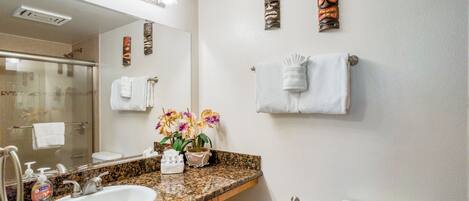 A bathroom with a granite countertop, white sink, and a glass shower enclosure.