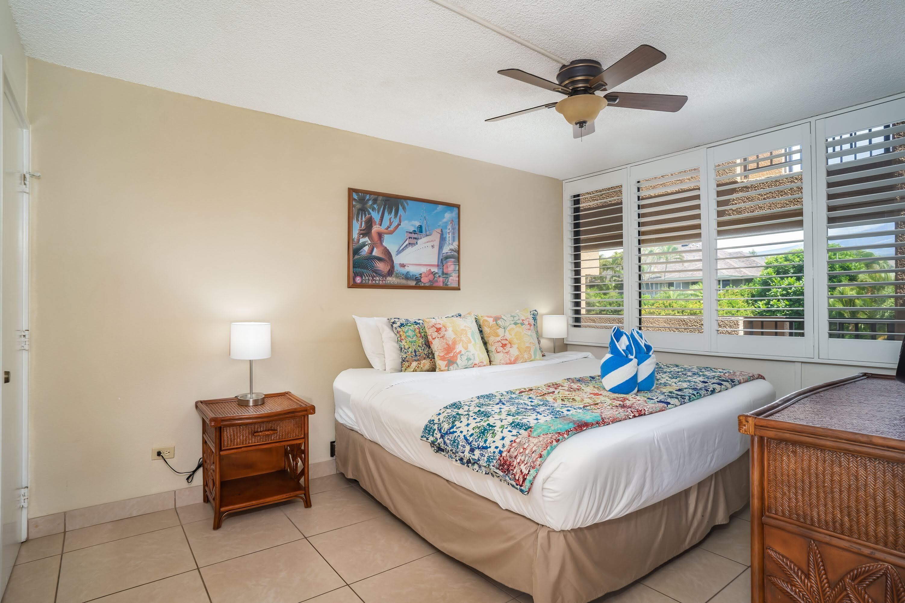 A bedroom with a bed, a nightstand, a ceiling fan, a window with blinds, and a painting on the wall.