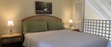 A neatly made bed with a quilted white cover, two bedside lamps, a nightstand with a drawer, and a painting of a waterfall on the wall.
