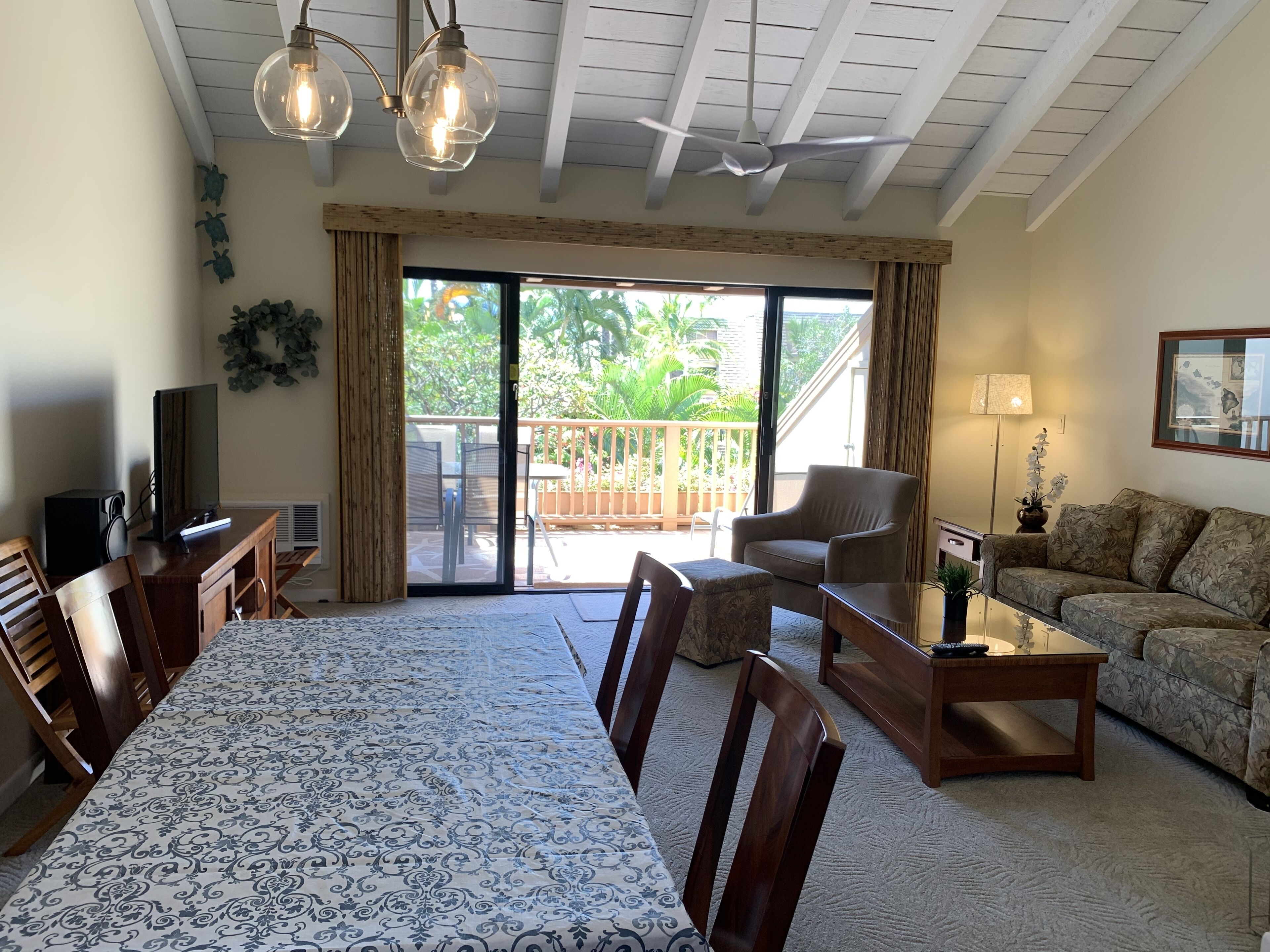 Een ruime woonkamer met een eettafel, stoelen, een bank en een balkon met uitzicht op groen.