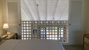 Un dormitorio con una cama, una mesita de noche con lámpara y vistas al exterior a través de un panel de madera.