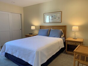 Un lit bien fait, recouvert d’une couette blanche, deux tables de chevet avec des lampes, une œuvre d’art florale encadrée accrochée au mur et une porte fermée.
