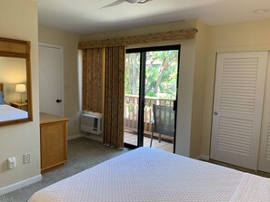 Une chambre d’hôtel comprenant un lit, une commode, un miroir, une fenêtre avec des rideaux, un appareil de climatisation et une porte-fenêtre coulissante donnant sur un espace extérieur.