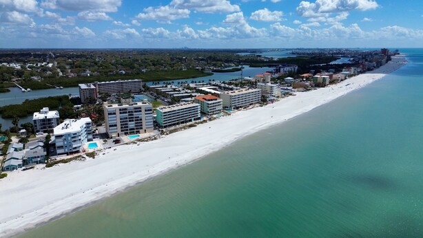 An aerial view of a coastal hotel area with multiple buildings, a beach, and a marina.