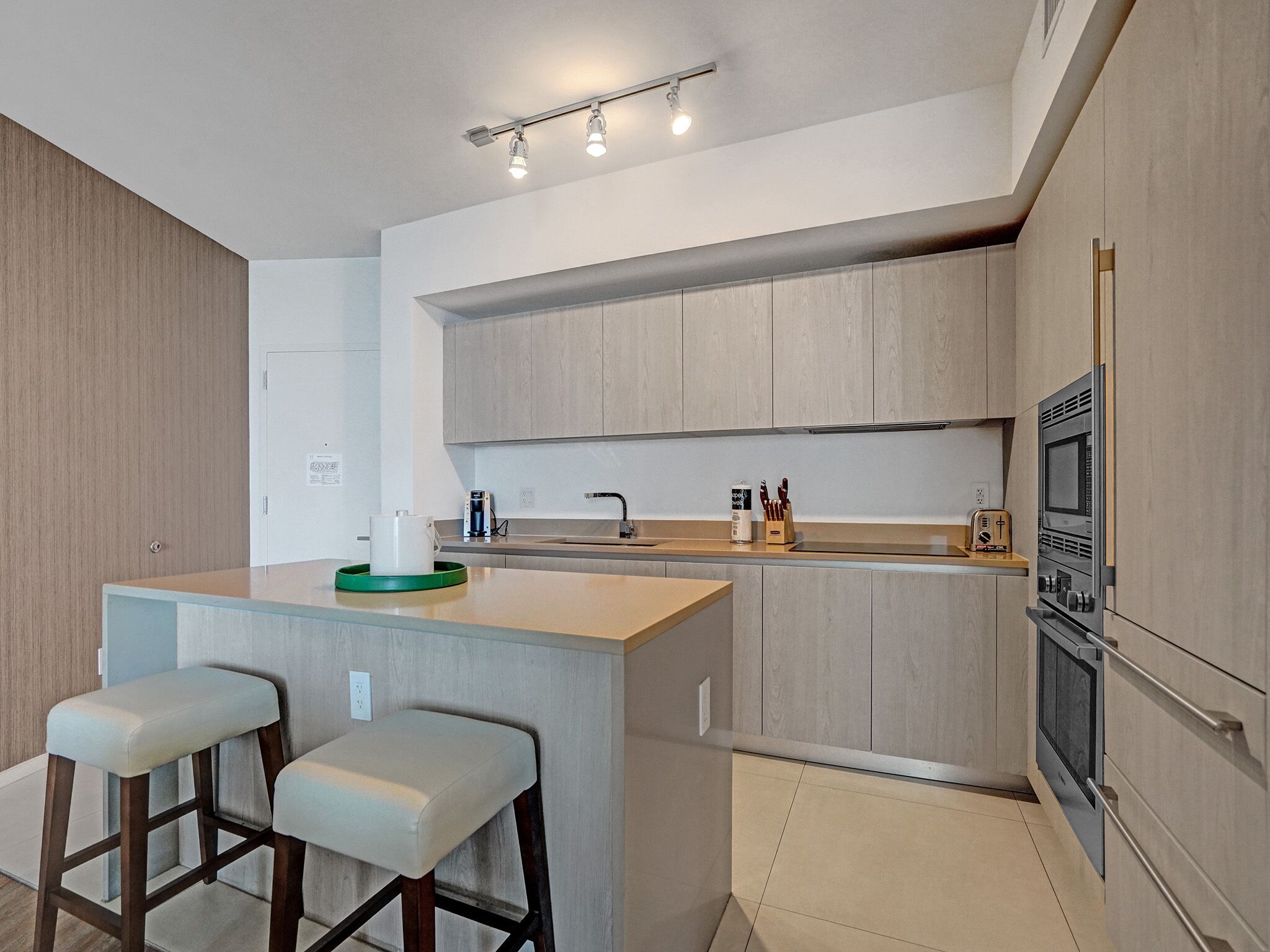 A modern kitchen with a central island, bar stools, a built-in oven, and a microwave.