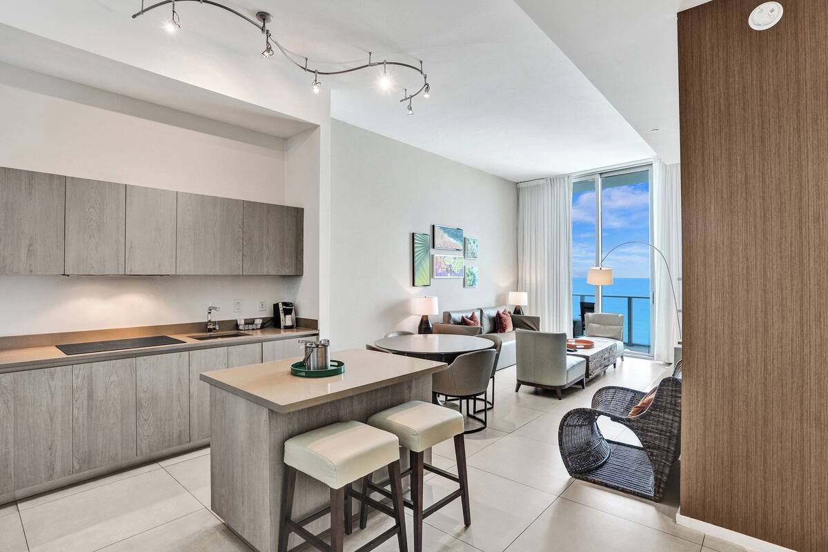 A modern kitchen with a central island, bar stools, and a dining area with a round table and chairs.
