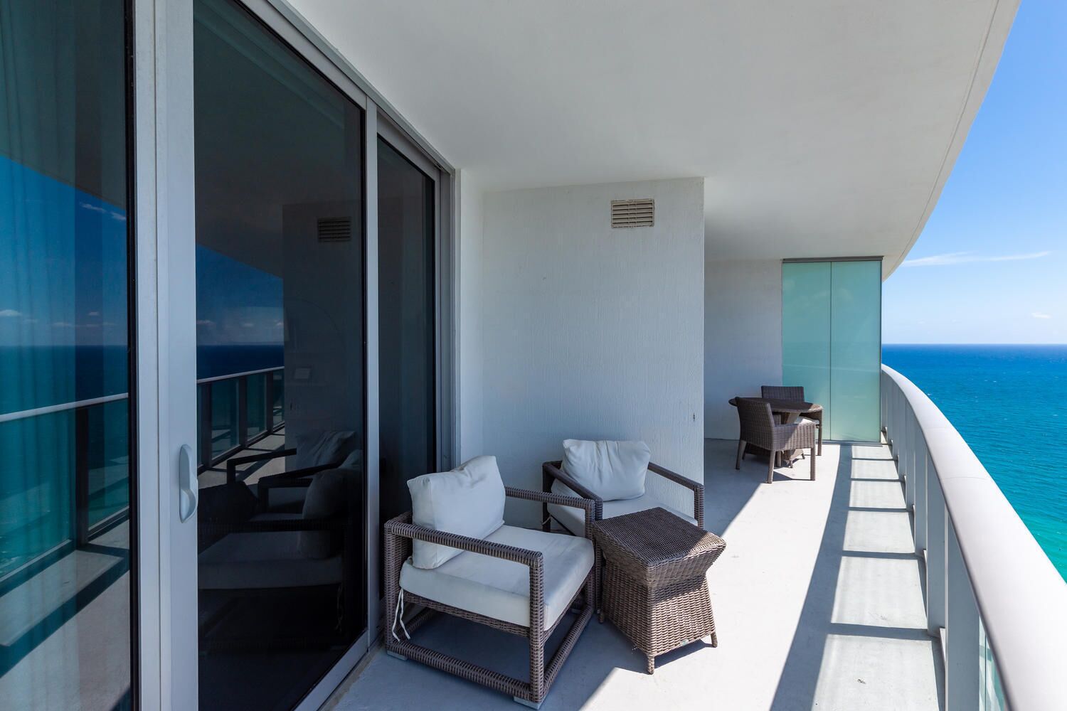 A balcony with wicker furniture, a glass door, and a view of the ocean.