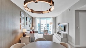 A modern hotel room with a large round table, a TV mounted on the wall, and a view of the cityscape through the windows. - Amazing Apartments at Lyfe Resort and Residences (Hollywood)