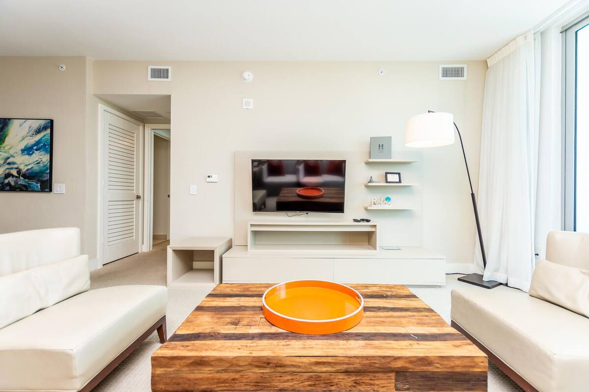 A modern living room with a flat-screen TV, white sofas, a wooden coffee table, and a floor lamp.
