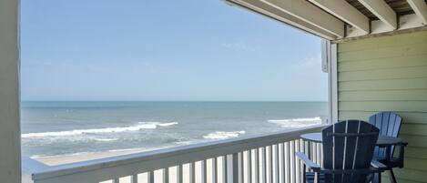 A balcony with a view of the ocean, featuring a table and two chairs.
