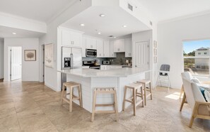 A spacious kitchen with white cabinetry, a large island with stools, and a view of the outside. - Seagrove Beachfront Condo + Pool & Stunning Views (Santa Rosa Beach)