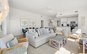A modern living room with a sofa, coffee table, and chairs, a dining area with a table and chairs, and a kitchen with appliances. - Seagrove Beachfront Condo + Pool & Stunning Views (Santa Rosa Beach)