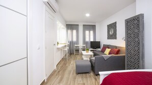 Una habitación de hotel moderna con un sofá gris, una cama roja, un televisor y una mesita con una planta.