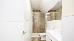 Un baño moderno con ducha de vidrio, inodoro blanco y un espejo grande.