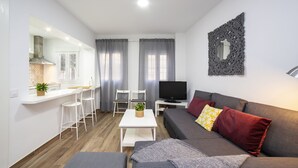 Una sala de estar moderna con sofá, televisión y un comedor con sillas y mesa.