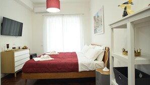 Ein Schlafzimmer mit Bett, Nachttisch, Lampe, Fernseher, Kleiderschrank und einem Fenster mit Vorhängen.