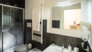 Ein modernes Badezimmer mit einer gläsernen Duschkabine, einem weißen Handtuchhalter, einem großen Spiegel und einem Fön an der Wand.