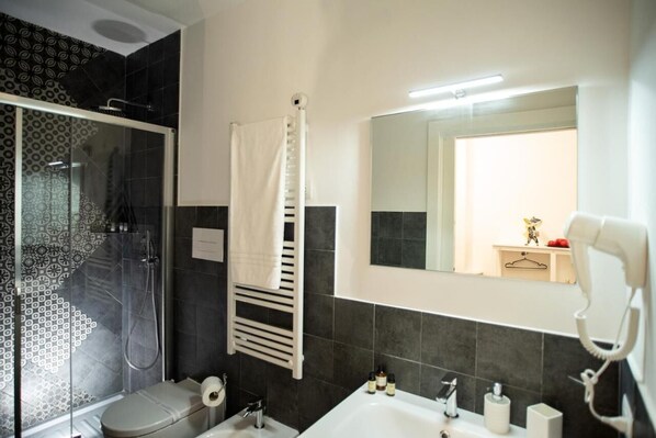 Un baño moderno con ducha de vidrio, toallero blanco, espejo grande y secador de pelo en la pared.