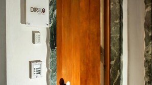 Eine Tür mit Holzverkleidung und einer weißen Wand, auf der ein Schild für ein Gästehaus, ein Klingel und ein Bedienfeld mit drei Tasten angebracht sind.