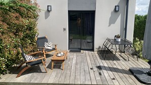 A modern outdoor deck with wooden furniture, a glass door leading to a patio, and a small table with a potted plant. - Studio Meublé 2 Personnes (Castelmaurou)