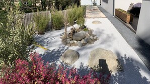 A garden with a gravel path, rocks, and pink flowering plants. - Studio Meublé 2 Personnes (Castelmaurou)