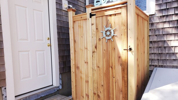 A wooden outdoor storage cabinet with a ship's wheel design, a white door, and a 'Beach' sign above it.