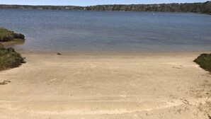 A sandy beach leading to a calm lake with a distant shoreline.