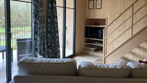 A wooden interior with a sofa, a TV stand, and a staircase.
