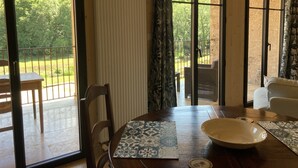 A room with a wooden table, chairs, a radiator, and large windows with curtains.