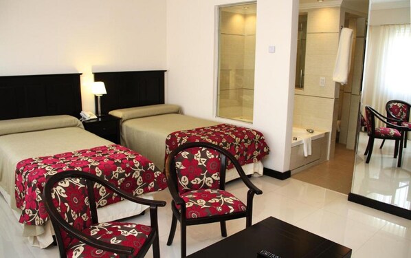 Une chambre d’hôtel avec deux lits, un bureau, une chaise et un grand miroir.