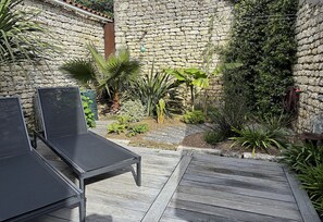 Une terrasse avec deux chaises longues noires, un mur en pierre et diverses plantes.