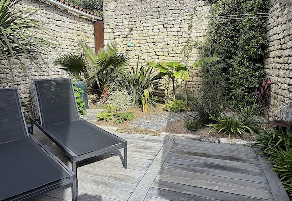 A patio with two black lounge chairs, a stone wall, and various plants.