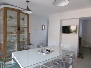 Un espace repas moderne avec une table en verre, des chaises blanches et un buffet en bois doté de portes en verre.