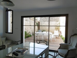 Ein modernes Zimmer mit einem Glastisch, weißen Stühlen und Blick auf eine Terrasse mit Steinmauer und Holzboden.