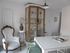 Ein Essbereich mit einem weißen Tisch, einem grünen Stuhl, einem Holzschrank mit Glastüren und einem weißen Stuhl mit geschwungener Rückenlehne.