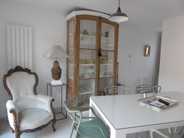 Un coin repas comprenant une table blanche, une chaise verte, un meuble en bois doté de portes en verre et une chaise blanche avec un dossier incurvé.