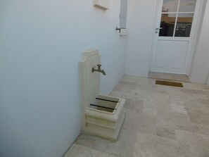 Ein schmaler Flur mit einer weißen Tür am Ende, eine kleine Stufe zu einer Tür, und ein gefliestes Parkett.
