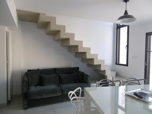 Un salon moderne avec un escalier en béton, un canapé vert foncé, une table à manger en verre et des chaises blanches.