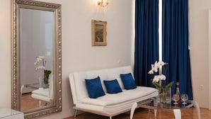A modern living room with a white sofa, a glass coffee table, a large mirror, and blue curtains. - Jagoda Apartman (Split)