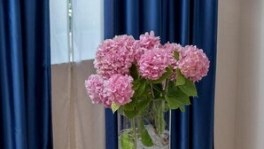 A table with a vase of pink flowers, a glass of water, and a blue cushion. - Jagoda Apartman (Split)