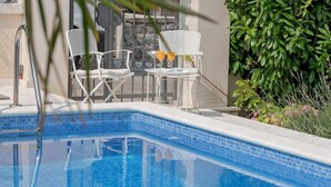 A swimming pool with a tiled edge, surrounded by white metal chairs and a lush green hedge. - Jagoda Apartman (Split)