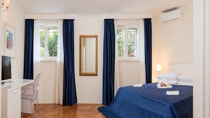A hotel room with a bed, a desk, a chair, a mirror, and two windows with curtains. - Jagoda Apartman (Split)