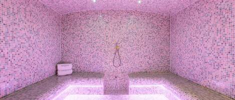A room with pink mosaic tile walls and floor, a bench, and a small white cabinet.